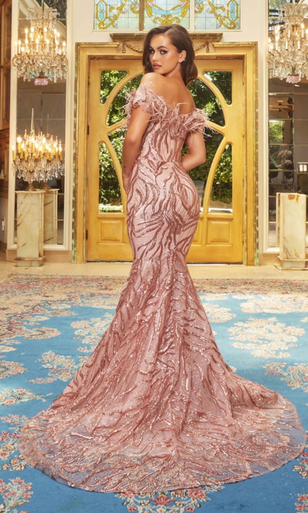 A woman poses in an ornate room wearing the Long Prom Dress PS22227 by Portia and Scarlett, a fitted off-the-shoulder mermaid gown with blush sequin embellishments and a sweeping train.